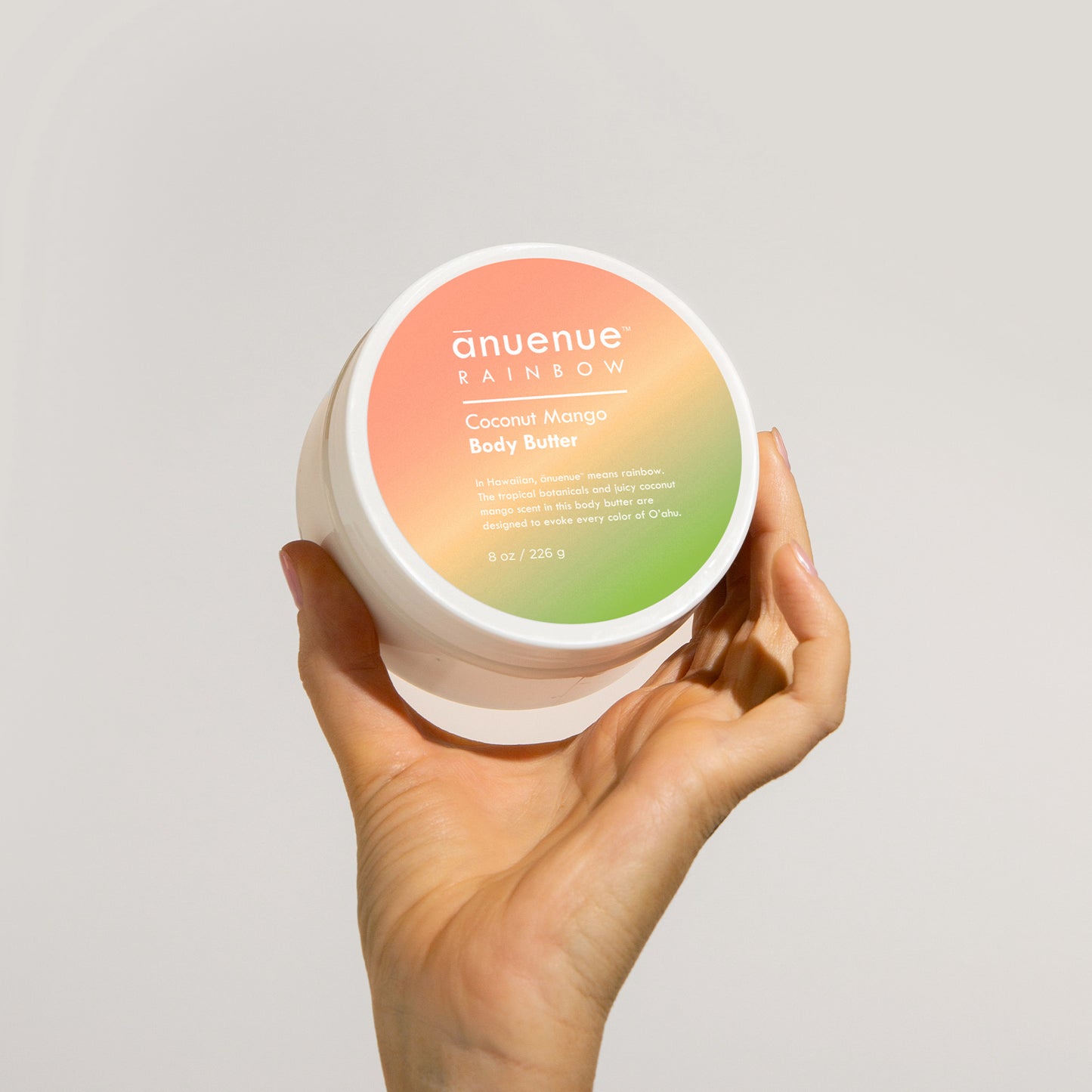 Hand holding an 8 oz Coconut Mango Body Butter in gradient rainbow jar